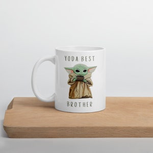 May include: White ceramic mug with a green alien character holding a cup. The text "YODA BEST BROTHER" is printed on the mug.