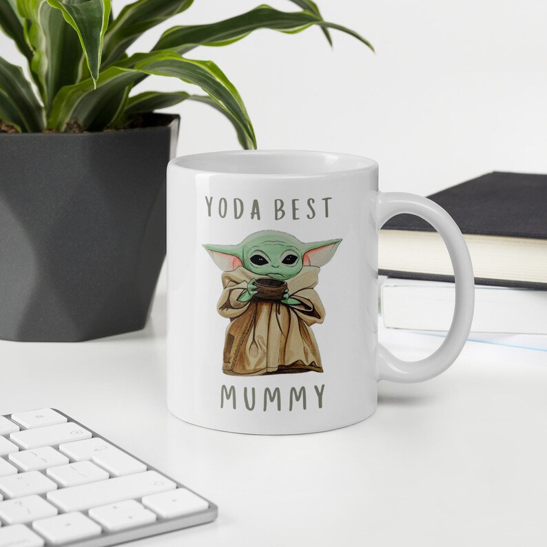 May include: White ceramic mug with a green cartoon character holding a cup. The text "YODA BEST MUMMY" is printed on the mug.
