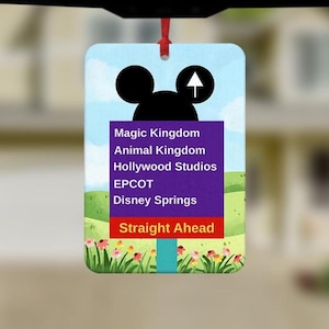 May include: A rectangular air freshener featuring a Mickey Mouse silhouette and an arrow. The sign lists Magic Kingdom, Animal Kingdom, Hollywood Studios, EPCOT, and Disney Springs, with "Straight Ahead" at the bottom. The background shows a blue sky and green hills.