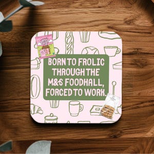 May include: A square coaster with a light pink background featuring a repeating pattern of line-drawn food items. A central olive green rectangle contains the text BORN TO FROLIC THROUGH THE M&S FOODHALL, FORCED TO WORK. Includes small images of Percy Pig sweets and biscuits.