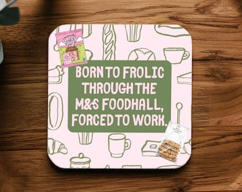 May include: A square coaster with a light pink background featuring a repeating pattern of line-drawn food items. A central olive green rectangle contains the text BORN TO FROLIC THROUGH THE M&S FOODHALL, FORCED TO WORK. Includes small images of Percy Pig candy and cookies.