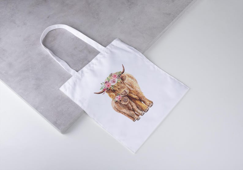 May include: White tote bag featuring a watercolor illustration of a Highland cow and calf adorned with floral crowns. The bag has a simple design with a rectangular shape and two white handles. The artwork is in shades of brown, pink, and green.