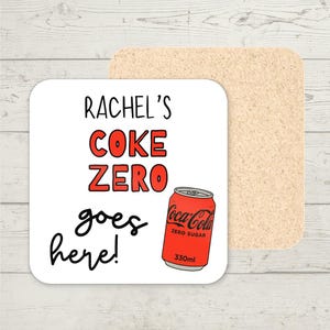 May include: A white square coaster with rounded corners. It has the text "RACHEL'S COKE ZERO goes here!" in black and red, and a red Coca-Cola Zero can. A second, plain cork coaster is behind it.