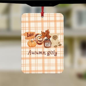 May include: A rectangular hanging air freshener featuring a light orange and white plaid pattern. The design includes a pumpkin, a cinnamon roll, a jar labelled Pumpkin Spice, and a teddy bear. Text reads Luke's Gilmore girls and Autumn girly.