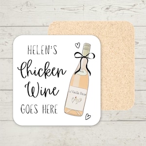 Può includere: Un sottobicchiere quadrato bianco con la scritta "Helen's Chicken Wine GOES HERE" in corsivo nero. Un'illustrazione di una bottiglia di vino con un fiocco nero e le parole "La Vieille Ferme" è sul sottobicchiere. Un secondo sottobicchiere in sughero è dietro.