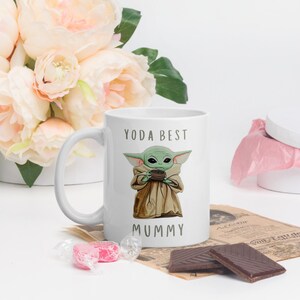 May include: White ceramic mug with a green alien character holding a cup. The text "YODA BEST MUMMY" is printed on the mug.