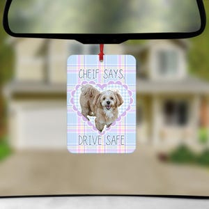 May include: A rectangular car air freshener hanging from a rearview mirror. The design features a light blue, pink, and white plaid background with a central purple heart frame containing a tan dog. Text reads: CHEIF SAYS, DRIVE SAFE.