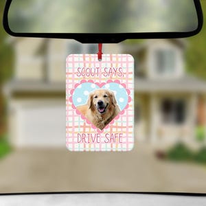 May include: A rectangular car air freshener hanging from a rearview mirror. The design features a light pink, yellow, and teal plaid background with a central light blue heart containing a golden retriever and the text SCOUT SAYS, DRIVE SAFE.