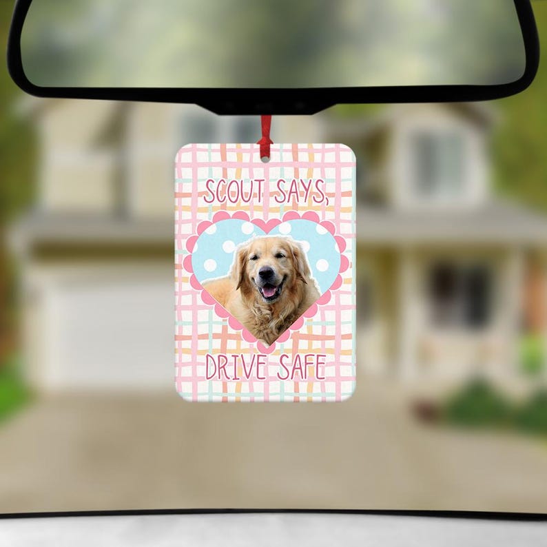 May include: A rectangular car air freshener hanging from a rearview mirror. The design features a light pink, yellow, and teal plaid background with a central light blue heart containing a golden retriever and the text SCOUT SAYS, DRIVE SAFE.