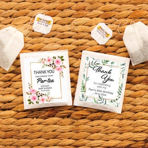 May include: Two tea bag packets with the text "Thank You" and "Par-tea" for a baby shower and birthday. The packets are decorated with floral and botanical designs. Twining tea bags are also visible.