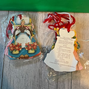 May include: Two vintage game cards featuring a red and white dress and a blue and white dress with a woman in each. The cards are part of a two-table progressive system tally game.