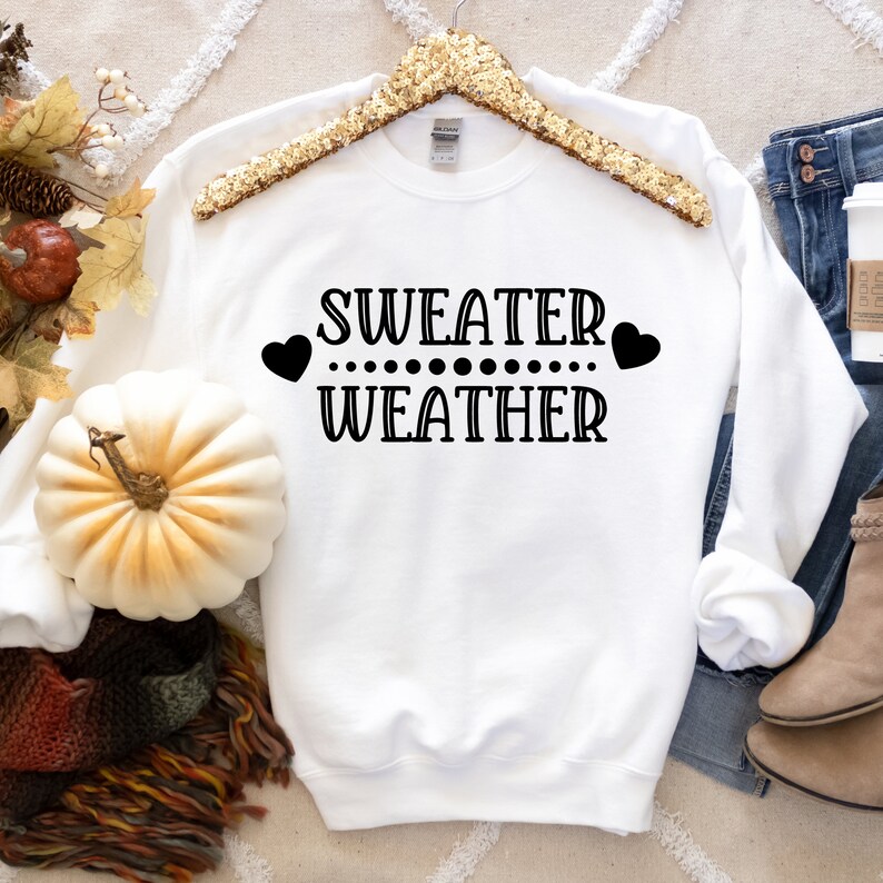 May include: White sweatshirt with black text that reads "SWEATER WEATHER" with two hearts and a row of dots between the words.