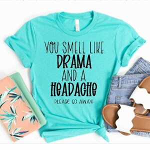 May include: A turquoise t-shirt with the text "You smell like drama and a headache. Please go away!" printed in black.