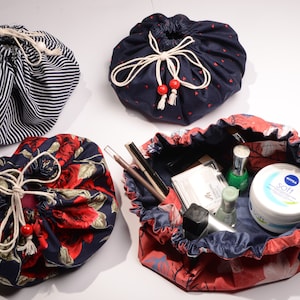 Könnte beinhalten: Vier Kosmetiktaschen mit Kordelzug in verschiedenen Mustern. Eine Tasche ist marineblau mit weißen Streifen, eine andere marineblau mit roten Herzen und eine dritte marineblau mit roten Rosen. Die vierte Tasche ist offen und zeigt Kosmetika.
