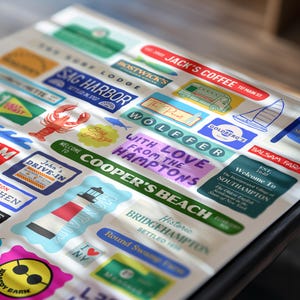 May include: A collection of colorful stickers featuring various designs and text. The stickers include images of a lobster, a sailboat, and a lighthouse, along with text such as "Jack's Coffee" and "Sag Harbor".