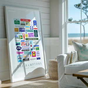 May include: A framed print featuring colorful signs and labels from The Hamptons, New York. The artwork includes various businesses and landmarks, such as Jack's Coffee, Sag Harbor, and Cooper's Beach. The print is displayed in a bright, coastal-themed room.