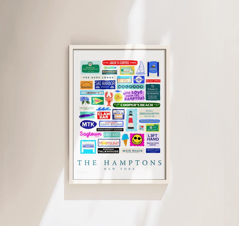 May include: A framed art print featuring a collage of colorful vintage-style labels and signs from The Hamptons, New York. The print includes text such as "Jack's Coffee", "Sag Harbor", and "Main Beach". The artwork is displayed on a white wall.