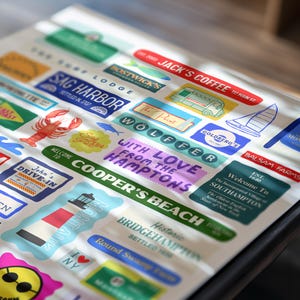 May include: A collection of colorful stickers featuring various designs and text. The stickers include images of a lobster, a sailboat, and a lighthouse, along with text such as "Jack's Coffee" and "Cooper's Beach."