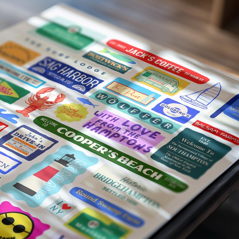 May include: A collection of colorful stickers featuring various designs and text. The stickers include images of a lobster, a sailboat, and a lighthouse, along with text such as "Jack's Coffee" and "Cooper's Beach."