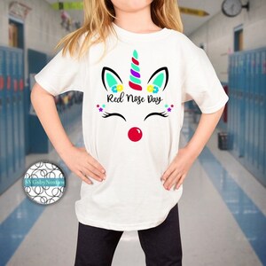 Pu&ograve; includere: Maglietta bianca con un design di unicorno con un naso rosso e il testo "Red Nose Day".