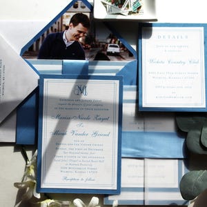 May include: Elegant wedding invitation suite featuring a photo, envelope, and cards in shades of white and blue. The invitation includes details and names in a classic font, with a blue border and ribbon.