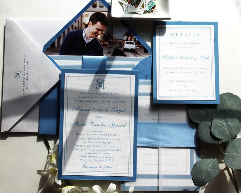 May include: Elegant wedding invitation suite featuring a photo, envelope, and cards in shades of white and blue. The invitation includes details and names in a classic font, with a blue border and ribbon.