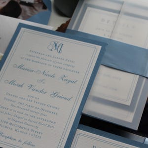 May include: Elegant wedding invitations with a light blue border and matching ribbon. The invitation includes the names of the couple, date, and location of the ceremony. The design features a monogram and detailed text.