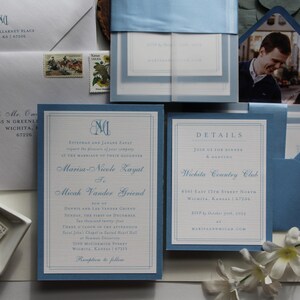 May include: Elegant wedding invitation suite in shades of blue and white. The set includes invitations, details cards, envelopes, and a photo. The invitations feature a monogram and the names of the couple. The details card provides event information.