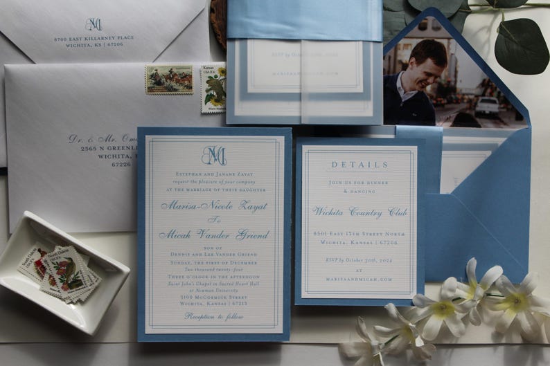 May include: Elegant wedding invitation suite in shades of blue and white. The set includes invitations, details cards, envelopes, and a photo. The invitations feature a monogram and the names of the couple. The details card provides event information.