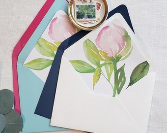 Pode incluir: Três envelopes com um design floral em aquarela. Os envelopes são em tons de azul, rosa e branco. O design floral apresenta uma flor rosa com folhas verdes.