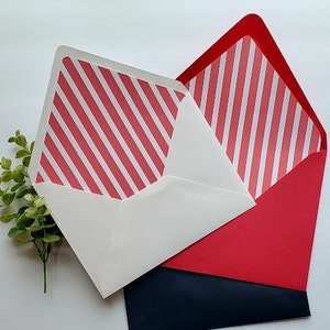 May include: Two folded cards with red and white striped patterns. The cards are layered on top of each other, with the top card folded in half and the bottom card folded in thirds. The bottom card is a dark blue color.