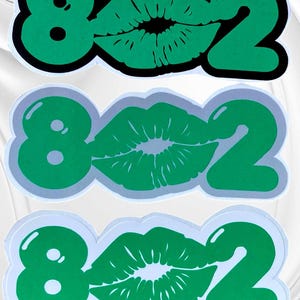 May include: Three green and black stickers with the number 802 and a green lip print in the middle. The stickers are on a white background.