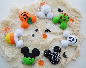 May include: A Halloween-themed felt garland featuring various shapes, including a pumpkin, mummy, zombie, candy corn, and Mickey Mouse-inspired characters. The garland is strung on white string and decorated with small plastic spiders and bats.