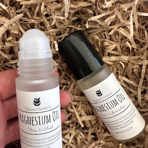 May include: Two clear glass roll-on bottles with black lids and white labels. The labels read "Qadosh Creations Magnesium Oil" and include the text "Stress & Mood" and "Pain & Inflammation".