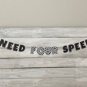 Op de afbeelding: Zwart-wit geblokt spandoek met de tekst "NEED FOR SPEED" op een witte houten achtergrond.