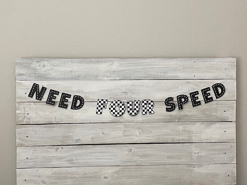 Op de afbeelding: Zwart-wit geblokt spandoek met de tekst "NEED FOR SPEED" op een witte houten achtergrond.