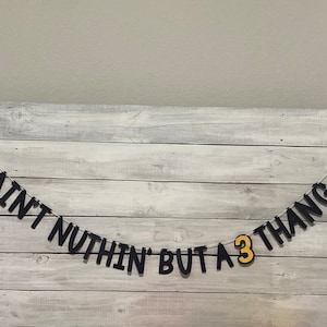 May include: A black and yellow banner with the text "Ain't nothin' but a 3 thang" and two yellow boombox cutouts on either end.