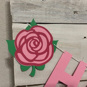 May include: A pink and green paper rose with a stem and leaves is part of a banner that says "Happy".