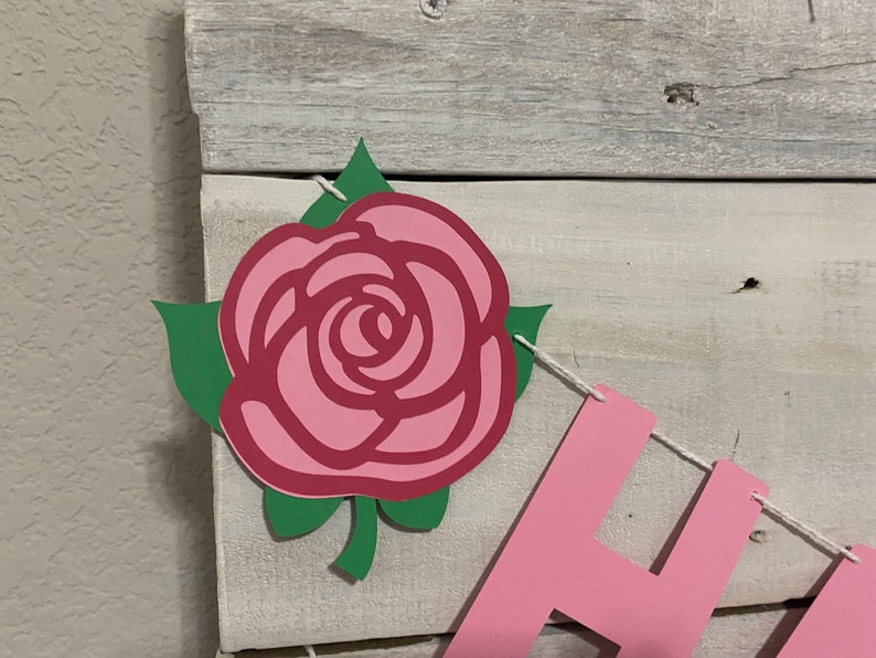 May include: A pink and green paper rose with a stem and leaves is part of a banner that says "Happy".