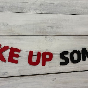 May include: Red and black felt letter banner that reads "Pike Up Some". The banner is strung on a white string and is hanging against a white wood background.