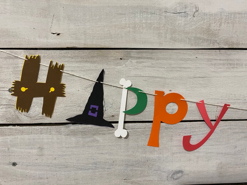 May include: A Halloween banner with the word "Happy" spelled out in colorful paper letters. The "H" is brown with yellow accents, the "a" is a witch's hat in black with purple accents, the "p" is a white bone, the "p" is green, the "y" is orange, and the "y" is red.
