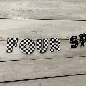 Op de afbeelding: Zwart-wit geblokt spandoek met de woorden "FOUR SPEED" in zwarte letters met witte stiksels.