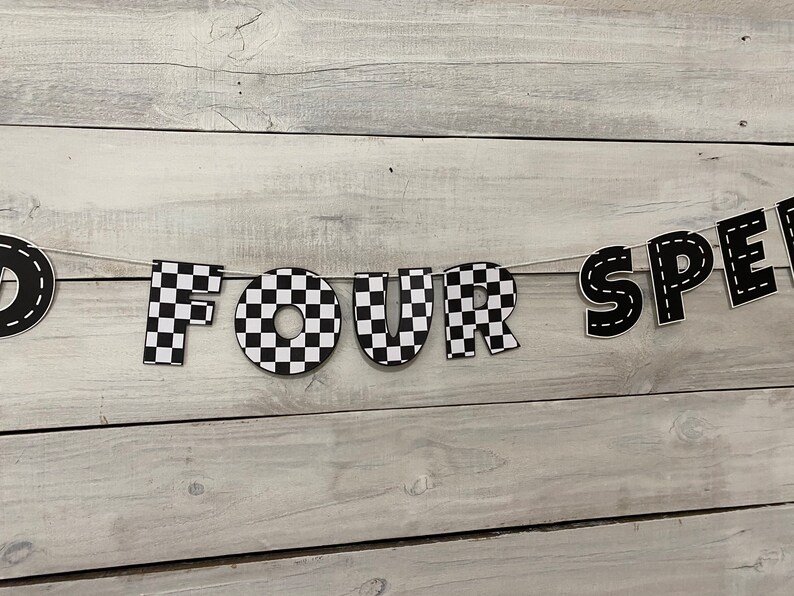 Op de afbeelding: Zwart-wit geblokt spandoek met de woorden "FOUR SPEED" in zwarte letters met witte stiksels.