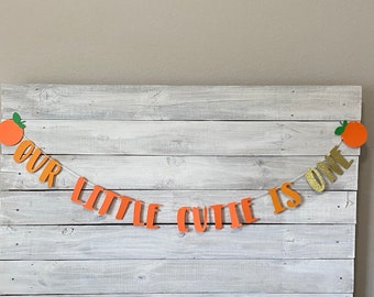 May include: Orange and gold banner with the text "Our Little Cutie Is One".