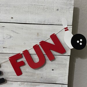 May include: A red and black banner with the word "FUN" in red letters and a bowling pin and ball. The banner is strung with white twine.