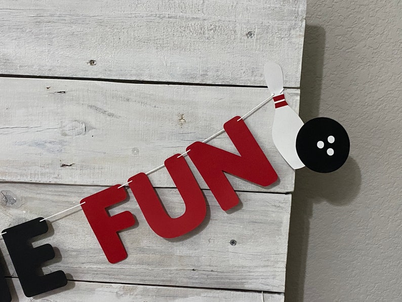 May include: A red and black banner with the word "FUN" in red letters and a bowling pin and ball. The banner is strung with white twine.