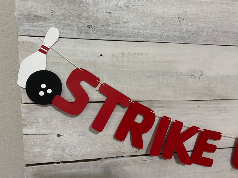 May include: Red felt banner with the word "STRIKE" in white letters. A white bowling pin with red stripes and a black bowling ball with white dots are attached to the banner.