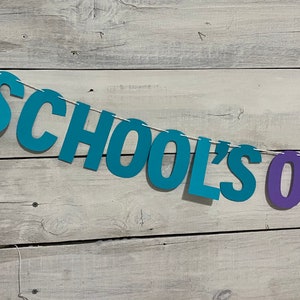 May include: A teal blue and purple paper banner with the text "SCHOOL'S OUT" hanging on a white wood background.