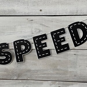 Op de afbeelding: Zwart-witte banner met het woord "SPEED" in grote letters. Elke letter is omlijnd met een witte gestikte lijn, die lijkt op een weg.