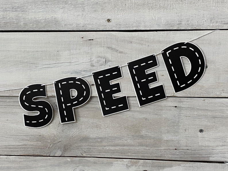 Op de afbeelding: Zwart-witte banner met het woord "SPEED" in grote letters. Elke letter is omlijnd met een witte gestikte lijn, die lijkt op een weg.